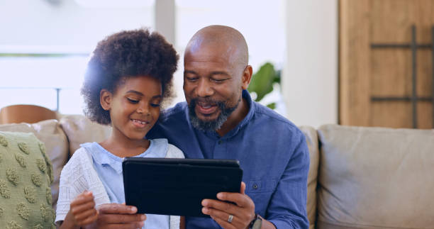 istock Father, daughter and tablet with smile on sofa for games, streaming or elearning in living room of home. Black family, man and girl child with touchscreen, happiness or technology for watching movie 1987146715