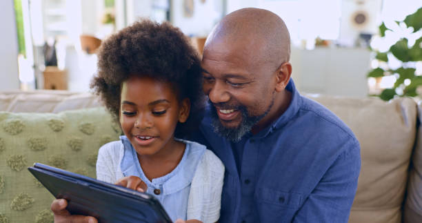 istock Dad, daughter and tablet with smile on sofa for games, streaming or elearning in living room of home. Black family, man and girl child with touchscreen, happiness or technology for watching movie 1987146719