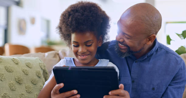 istock Father, daughter and tablet with smile on sofa for games, streaming or elearning in living room of home. Black family, man and girl child with touchscreen, happiness or technology for watching movie 1987146721