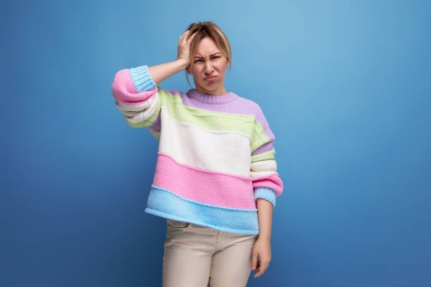 istock distressed blond woman in casual look holding her head on blue background 1987152262