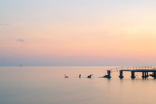 Key West sunset long exposure. The sky is pink and the sea is calm. A single Heron waits for fish on a wooden post