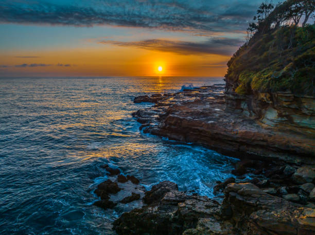 istock Sunrise over the calm ocean with light cloud and rocks 1987203037