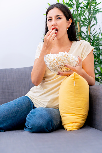 Young woman relaxing and eating popcorn on a comfortable couch at home.