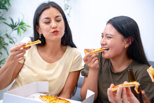 Two women share a moment of happiness while enjoying pizza slices together at home.