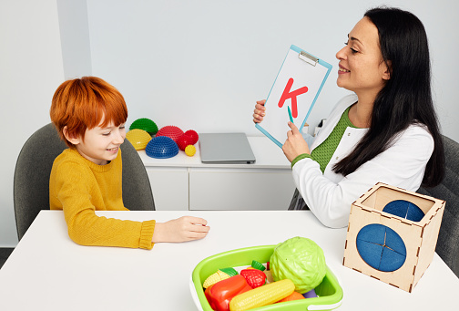 Red-haired boy during speech therapy session. Speech therapist teaching child to pronounce letter k