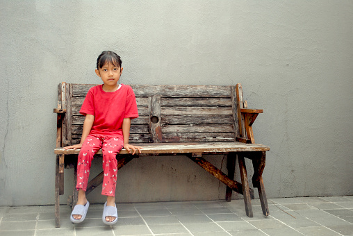 Little Indonesian girl is sitting on the wooden bench.