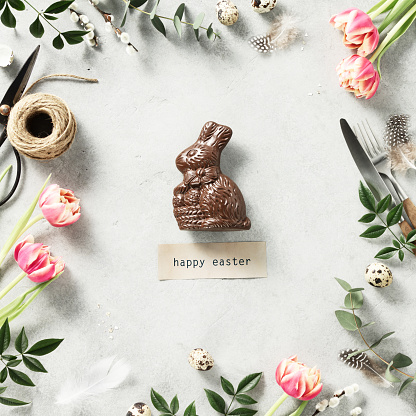 Easter background with Easter Chocolate Bunny spring flowers and cutlery on light grey background top view flat lay copy space square composition