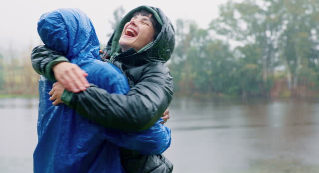 Camping, love and a couple hugging in the rain while outdoor in nature together for romance or adventure. Smile, freedom or travel with a man and woman bonding while hiking in wet winter weather