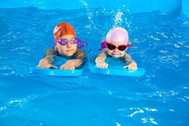 istock Two little girls learning how to swim in swimming pool using flutter boards 1987243553