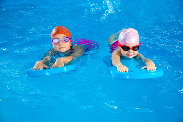 istock Two little girls having fun in pool learning how to swim using flutter boards 1987243562