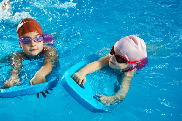 istock Two little girls learning to swim in indoor pool with pool board 1987243576