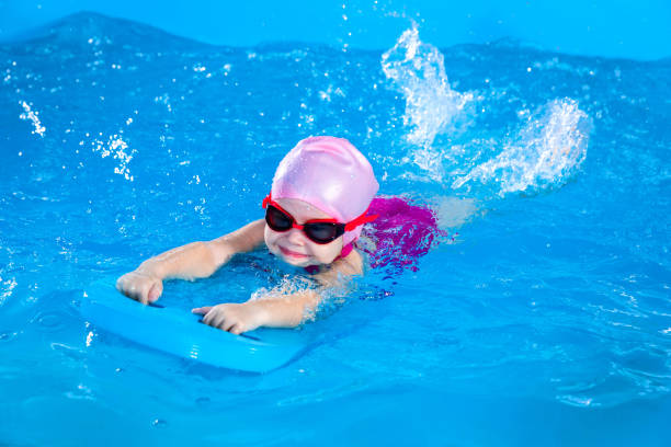 istock Preschool cute girl learning to swim in indoor pool with flutter board 1987243577