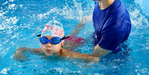 istock Trainer teaching little boy how to swim in indoor pool with pool floating board 1987243591