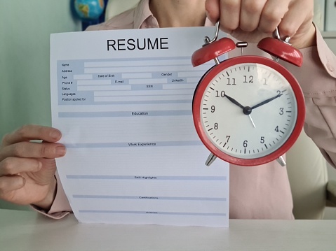 Close up of hands holding red alarm clock and resume with focus on time management, deadline, and recruitment concept. Suitable for business, tourism, and creative ideas.
