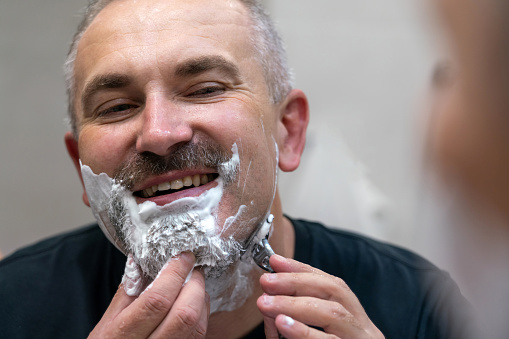 Handsome man shaving his beard in a bathroom