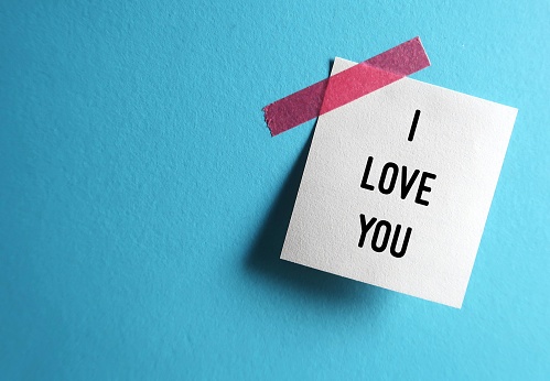 Note stick on blue background with text I LOVE YOU, concept of self talk to remind oneself to feel loved and worthy, or a romantic love confession, telling someone you have a crush on them