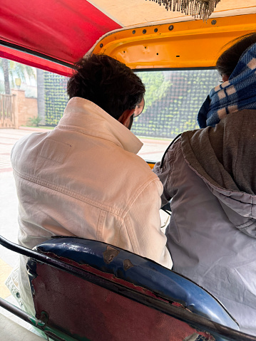 Stock photo showing the backs of a passenger and an auto rickshaw driver as seen by a passenger on a journey in the back seat.