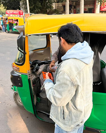 New Delhi, India - January 2, 2024: Stock photo showing close-up view of parked auto rickshaw driver being paid by passenger at end of a ride.