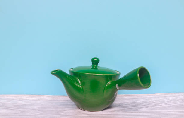 istock Green porcelain teapot for making tea on gray table and isolated on a blue background with copy space 1987272230