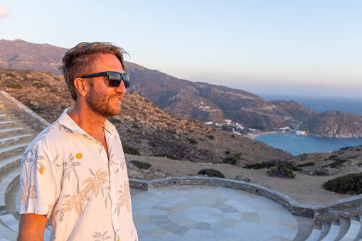 He looks at the beautiful traditional greek town on the hill on Ios Island, Greece.