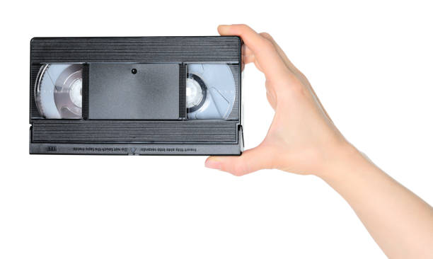 istock Woman hand holds a retro old analog video cassette, isolated on white background, retro things concept 1987281341