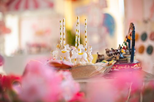 a cake topped with some lit candles before blowing out the cake, on a rustic wooden table full of confetti, party horns and streamers, with a filtered effect