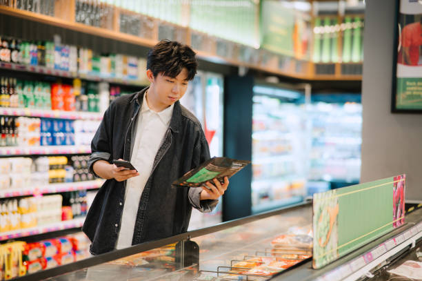 istock Asian Chinese Student Looking At Smartphone While Choosing Items In Supermarket. 1987290949