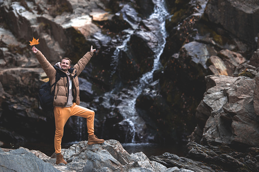 Young hiker man standing next to a waterfall with outstretched arms,