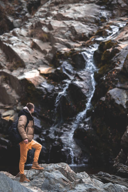 istock Young hiker man with backpack standing near to a waterfall and looking at it 1987300097