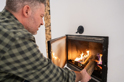 Mid-adult Caucasian man put an log into fireplace, at his home