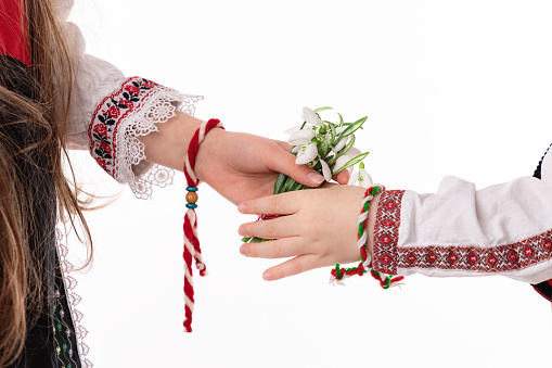 Bulgarian kids boy and girl in traditional folklore costumes with spring flowers snowdrop and handcraft wool bracelet martenitsa symbol of Baba Marta
