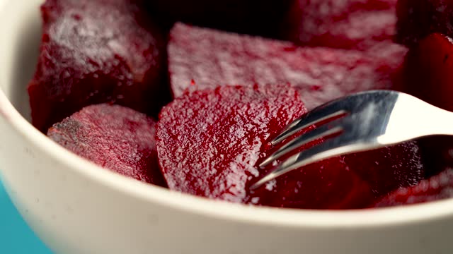 Dietary cooked boiled red beets with a steel fork in a ceramic bowl on a colored blue background. Rotation