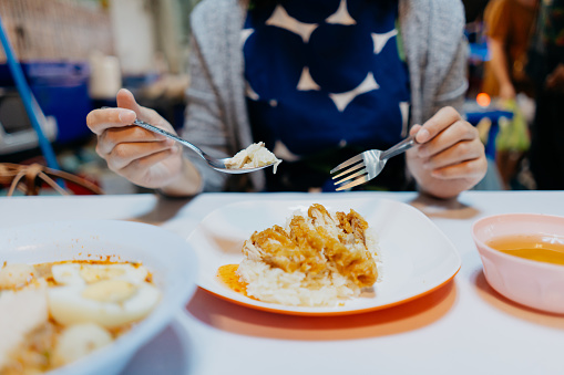 Close up shot of an Asian female tourist enjoying street food chicken rice Khao Man Gai at a night market in Bangkok