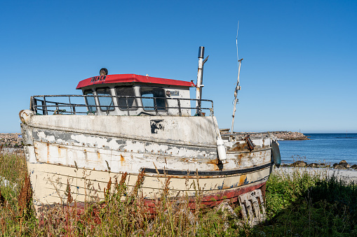 An aged boat rests on sandy shores, revealing its deck and engine