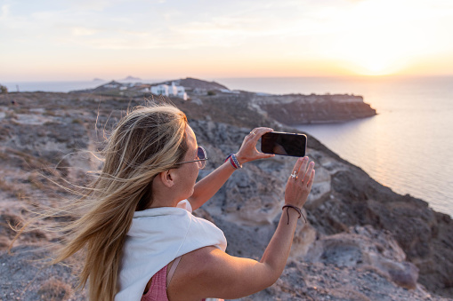 As the sun dips below the horizon, a tourist in Santorini captures the magic of the moment with a radiant sunset selfie. Golden hues paint the sky, creating a stunning backdrop for this unforgettable travel snapshot.