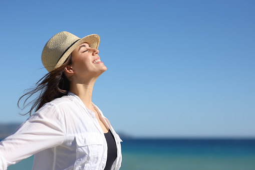 Happy woman on the beach breathing with hat