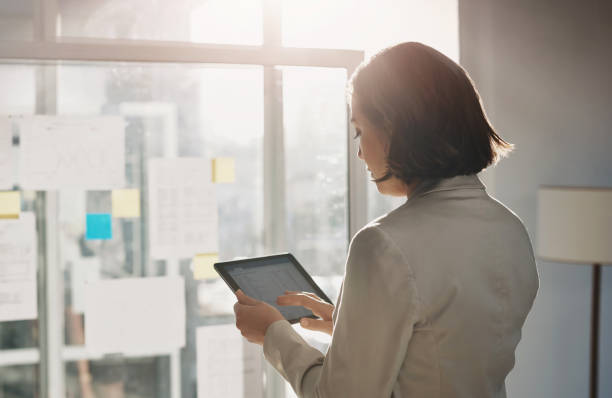 istock Woman, tablet and glass board in office, planning and click to review for problem solving. Business person, employee and digital touchscreen with typing for stats, analysis or app for finance report 1987369610