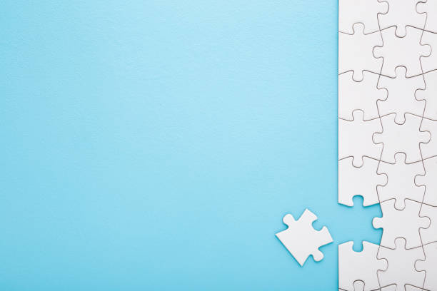 istock Unfinished white puzzle with last one piece on light blue table background. Pastel color. Closeup. Empty place for text. Top down view. 1987387044