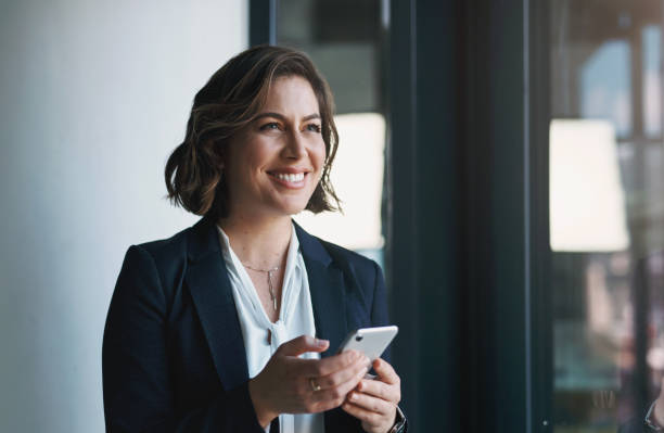 Business woman, phone and thinking by window for human resources ideas, solution and happy communication. Professional worker or employee with inspiration for mobile chat, online networking and email