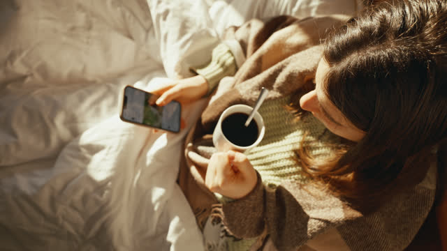 SLO MO Top View of Young Woman Checking Social Media on Smartphone while Having Black Coffee Sitting on Bed in Morning