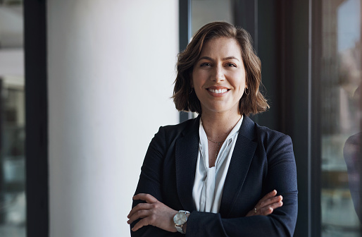 Confident mature woman with crossed arms in formal clothing with copy space looking at camera. Happy smiling mid adult woman standing against grey background. Portrait of beautiful positive businesswoman.