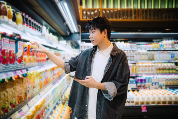 istock Asian Chinese Student Looking At Smartphone While Choosing Items In Supermarket. 1987407504