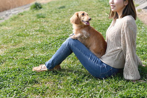 Young Asian woman sitting on the lawn with her beloved dog (miniature dachshund)