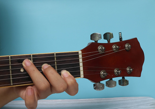 C basic major keys guitar tutorial series. Closeup of hand playing C major chord on guitar isolated on blue background