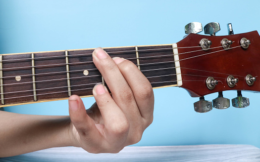 G basic major keys guitar tutorial series. Closeup of hand playing G major chord on guitar isolated on blue background