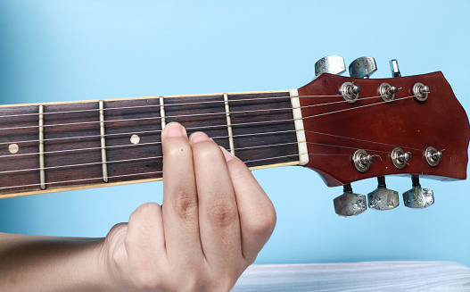 E basic major keys guitar tutorial series. Closeup of hand playing E major chord on guitar isolated on blue background