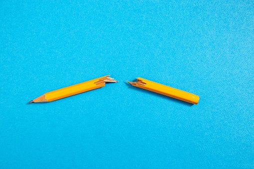 Orange wooden crayon, snapped in two, on blue paper background
