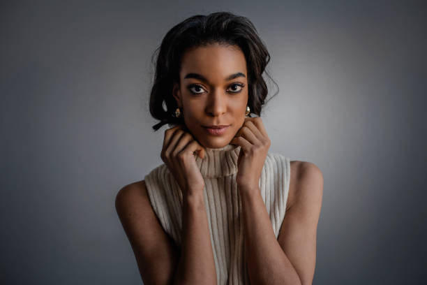 Smiling African American female portrait. Black haired woman looking at camera and smiling against gray background. Copy space. Her hand by her face.