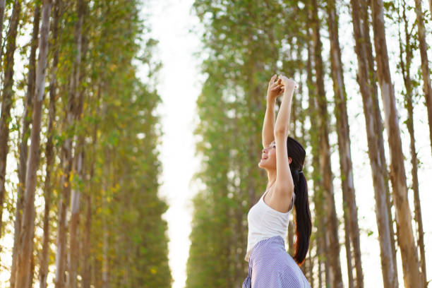 Asian girl in pink dress jumping with arms raised on nature path. Happiness, childhood energy, and excitement in outdoor learning and play experience in lush green environment.