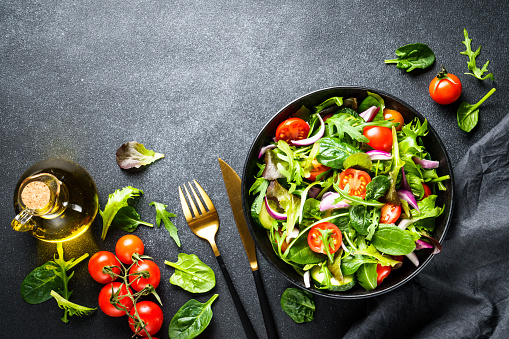 Green Salad with salad leaves and vegetables at black background. Top view with copy space.